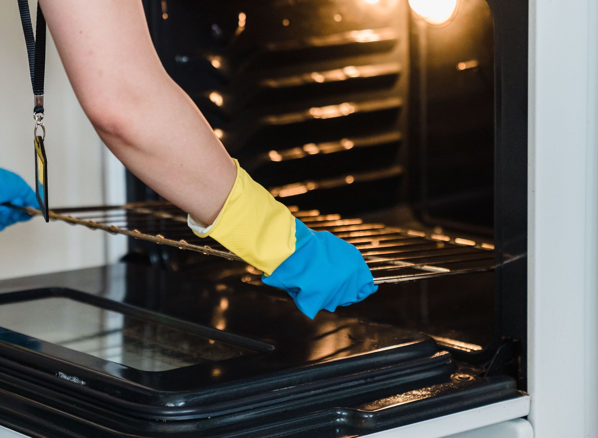 Adult woman cleaning an oven using protective rubber gloves indoors.