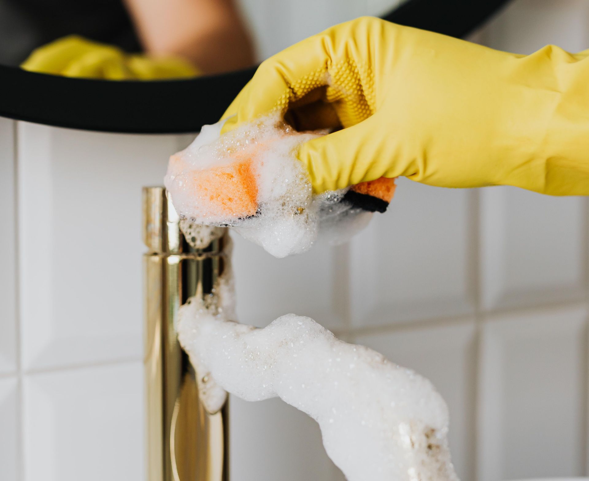 Anonymous person washing golden shiny faucet and sink in bathroom while wearing yellow latex glove during household care routine work